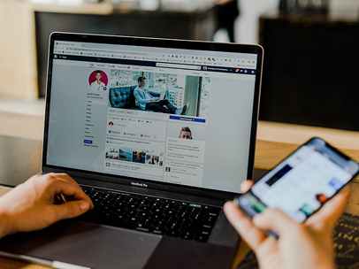 A laptop with a person's hand on the keyboard, and the other hand holding a phone.